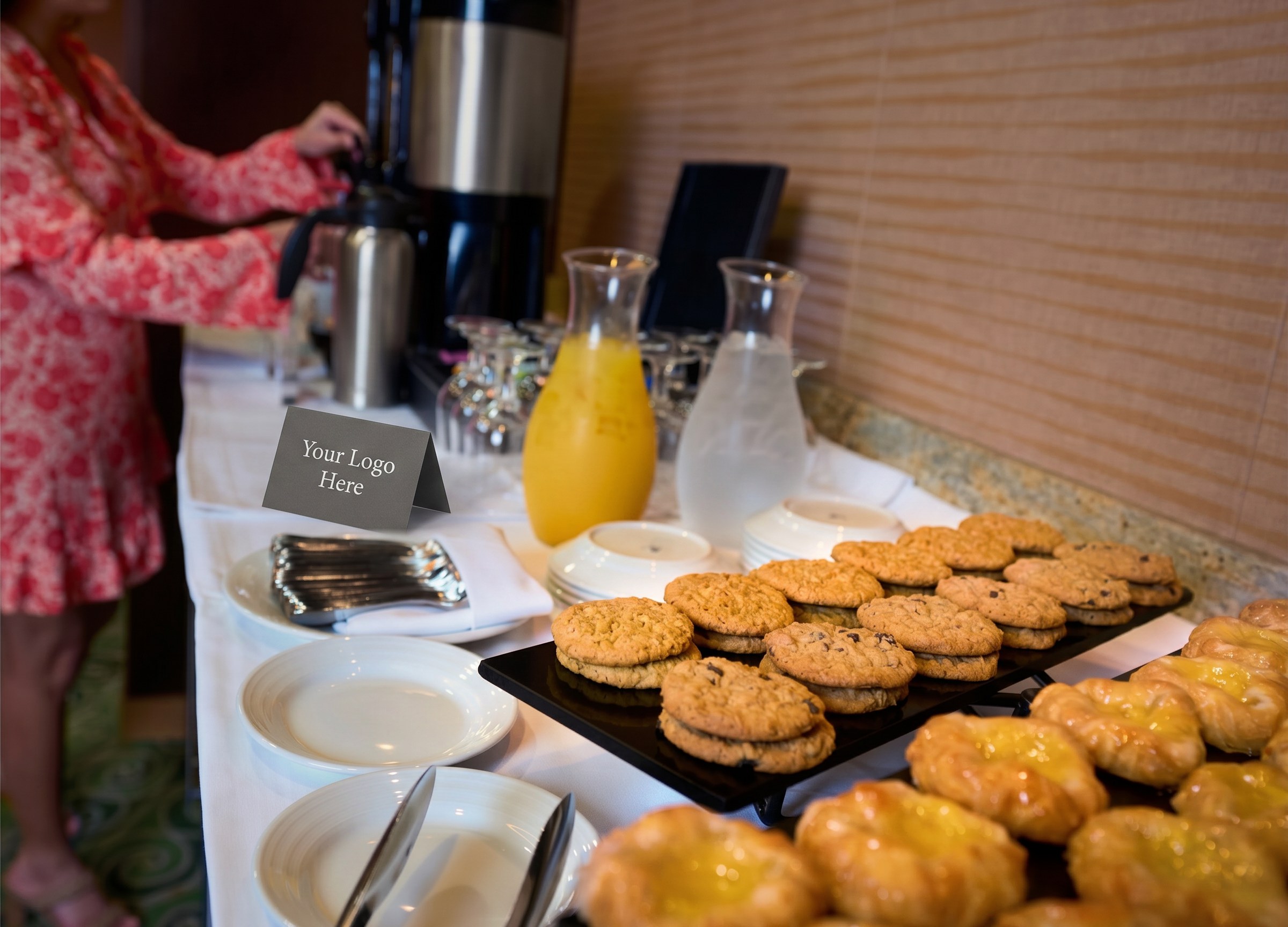 Coffee break service with pastries, juice, coffee carafes, and a tented 'Your Logo Here' card on the table